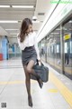 A woman in a skirt and shirt is walking on a subway platform.