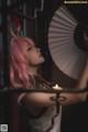 A woman with pink hair holding a fan and a candle.