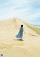 A woman in a blue dress walking up a sand dune.