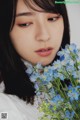 A woman holding a bunch of blue flowers in her hand.