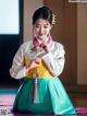 A woman in a green and yellow hanbok is holding a key.