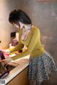 A woman in a yellow shirt and blue skirt washing an eggplant.