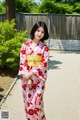 A woman in a red and white kimono standing on a sidewalk.