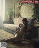 A naked woman sitting on a rug in a living room.