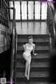 A woman in a white bodysuit sitting on a set of stairs.