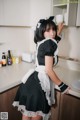 A woman in a maid outfit standing in a kitchen.